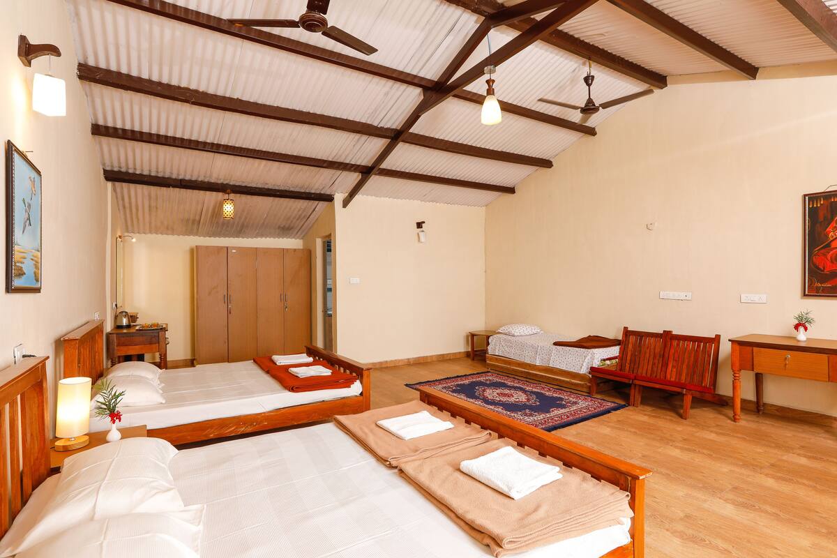 A room with two beds, a wooden desk, a bench, and a ceiling fan.