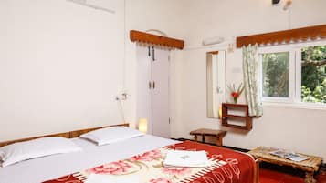 A bedroom with a bed, a bedside table, a window with a view of greenery, and a mirror on the wall.