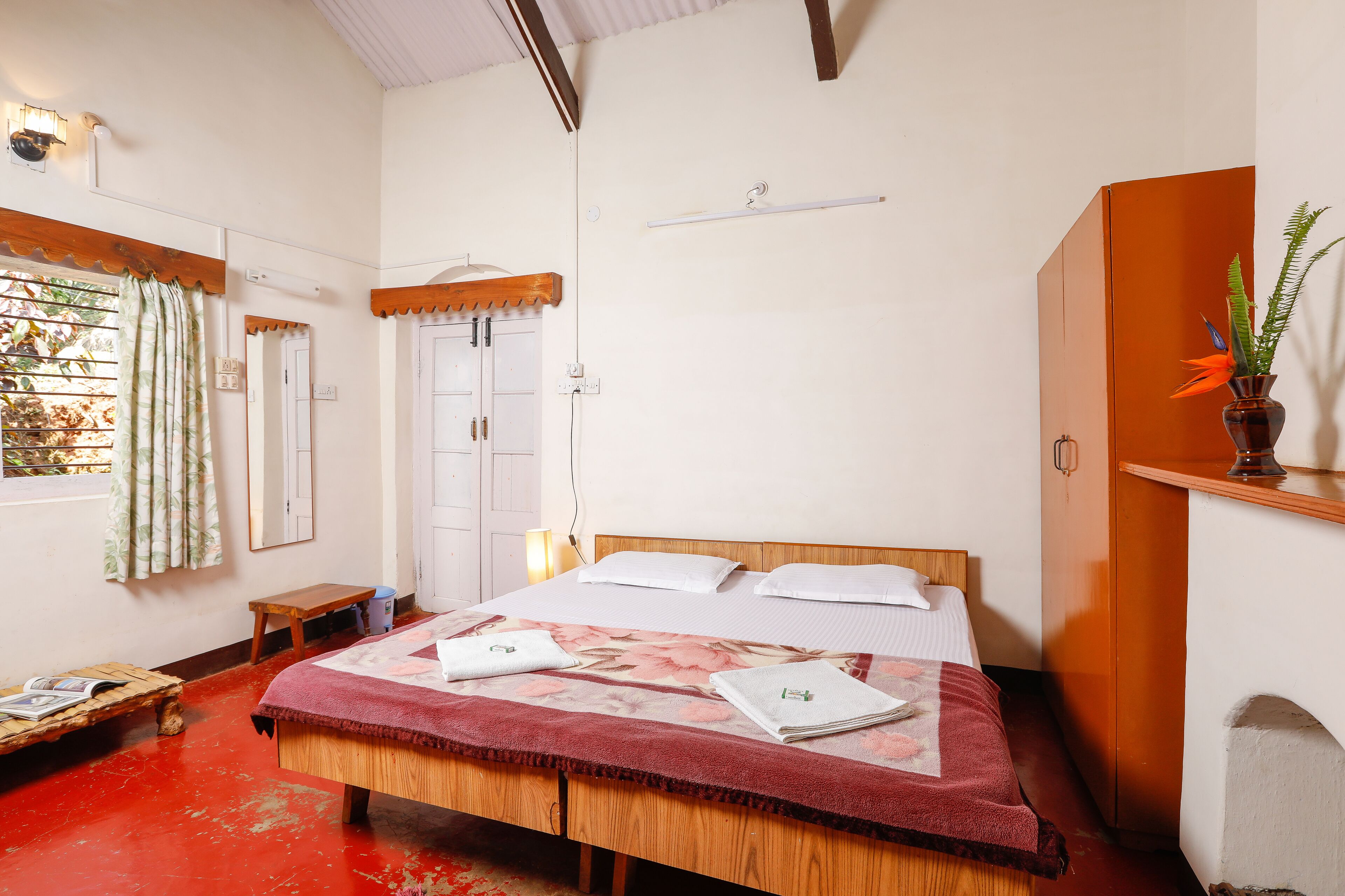 A room with a wooden bed, a bench, a small table, and a potted plant.