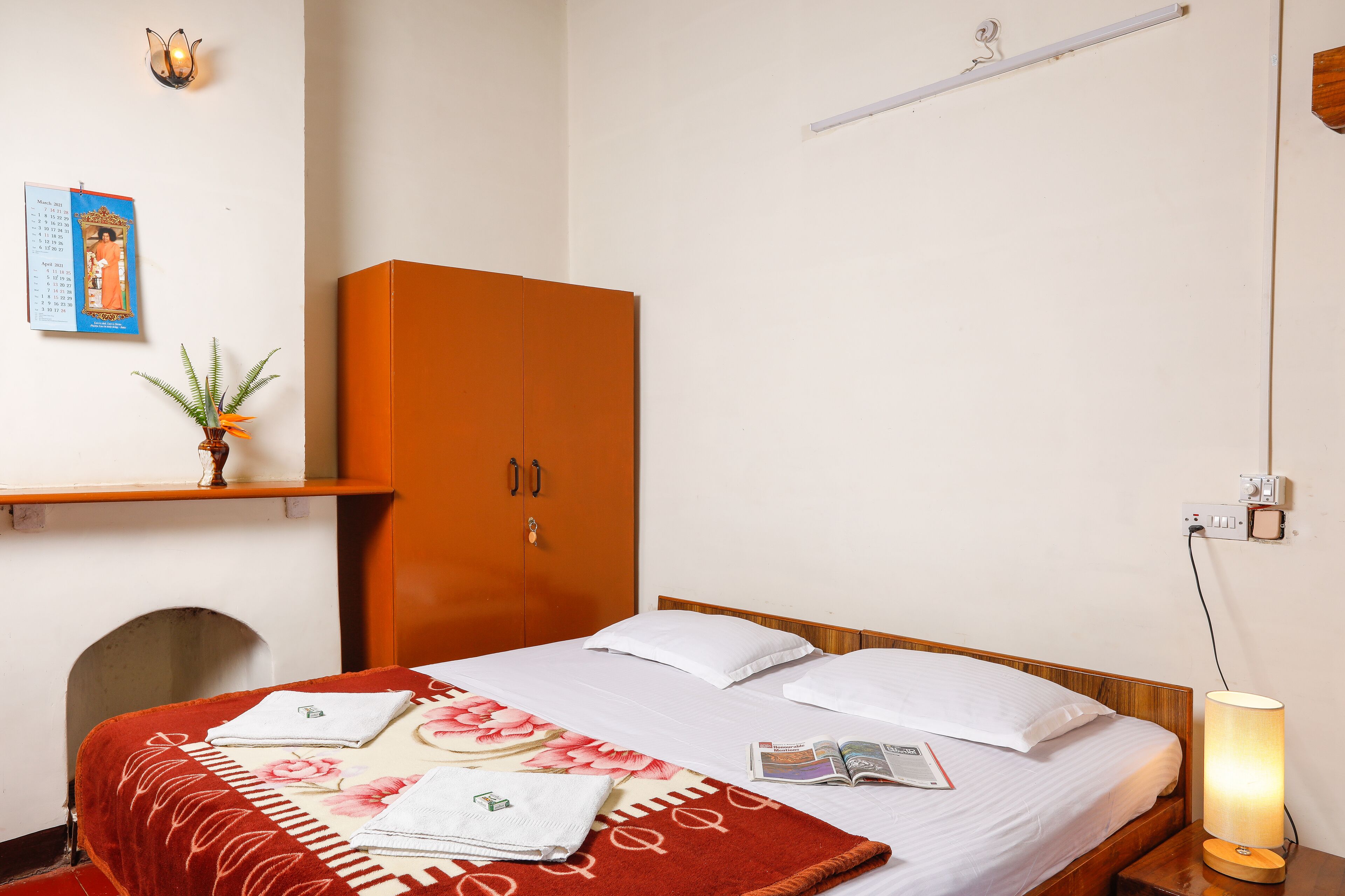 Une chambre d’hôtel avec un lit, une armoire, une étagère avec une plante et un calendrier mural.