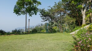 Un parque con césped, un columpio, árboles y un farol.