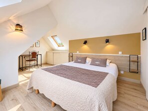 A bedroom with a large bed, a desk, and a skylight.