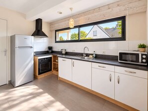 A modern kitchen with a refrigerator, oven, microwave, and a window with a view of a house.
