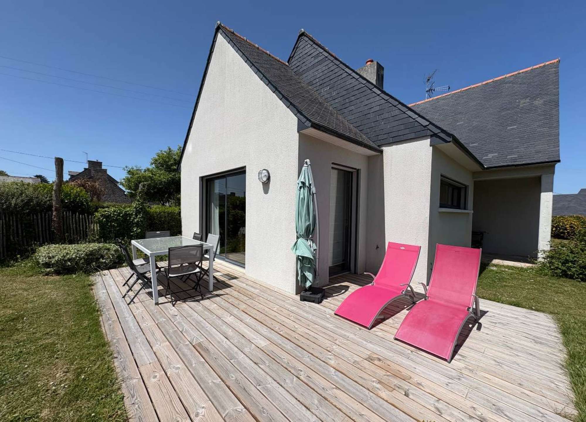 A modern house with a deck, a dining area, and two red sun loungers.