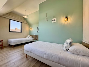 A bedroom with a large bed, a smaller bed, a window, and a wall-mounted light fixture.