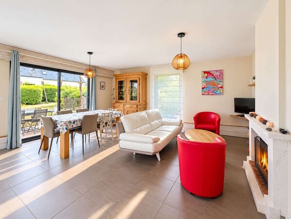 A modern living room with a fireplace, a dining area with a table and chairs, and a red accent chair.