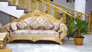 Un canapé luxueux agrémenté de motifs dorés complexes, un sol en marbre et un escalier avec des rampes dorées.