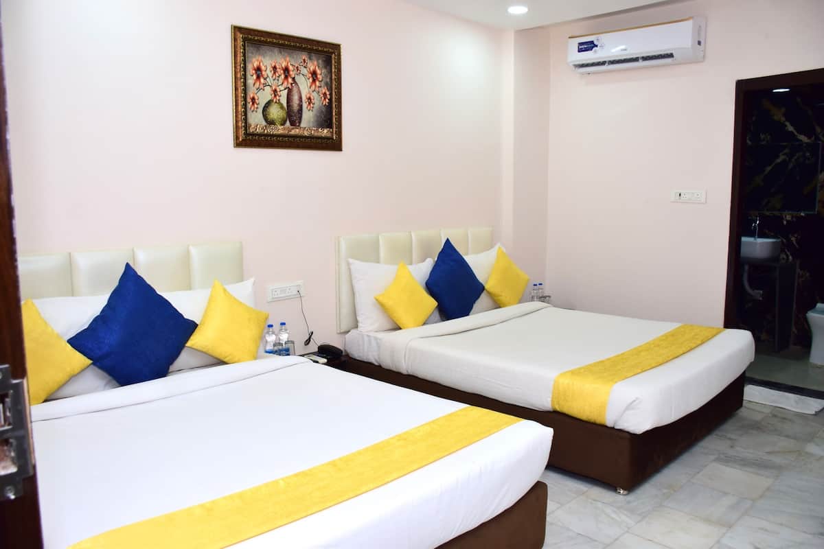 Two beds with white and yellow bedding, a painting on the wall, and an air conditioning unit.