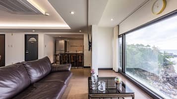 Una sala de estar moderna con un sofá de cuero, una mesa de centro con cristalería y un amplio ventanal con vistas a un litoral rocoso.