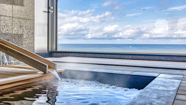 Un área de aguas termales con una terraza de madera y vista al mar.