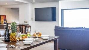 Un comedor con una mesa dispuesta para dos, que incluye una botella de vino, una piña y una copa de vino blanco.