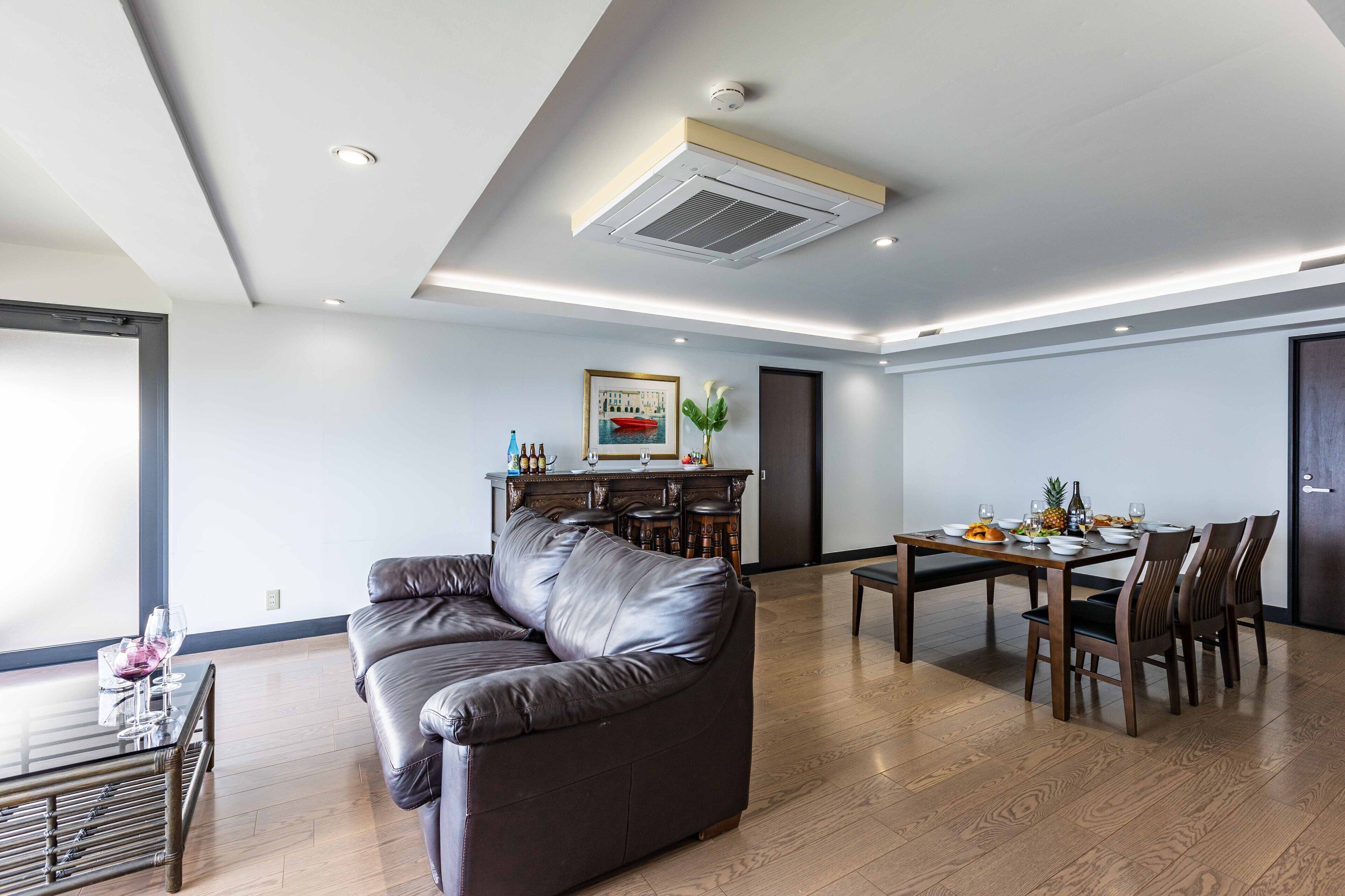 Una sala moderna con un sofá de cuero, una mesa de comedor y sillas. Hay una zona de cocina con un refrigerador y una mesa de comedor con comida y bebidas.