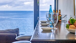Una mesa de comedor con platos, vasos y botellas, frente a una vista del océano.