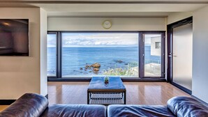 Un salón moderno con un ventanal grande con vistas al mar, suelo de madera y una mesa de centro de cristal.