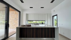 A modern kitchen with a central island, a large window, and a view of greenery outside. - Res & Campo (Pinhal Novo)