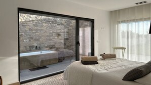 A bedroom with a large sliding glass door leading to a stone wall and a bathroom. - Res & Campo (Pinhal Novo)