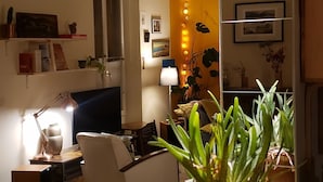 A living room with a yellow table, a white sofa, and a TV. There are plants on the table and a lamp on the side. - Havre de Paix (Montreuil)