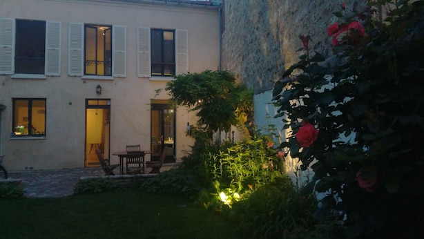 A building with a garden, a patio with a table and chairs, and a door leading to an interior space. - Havre de Paix (Montreuil)