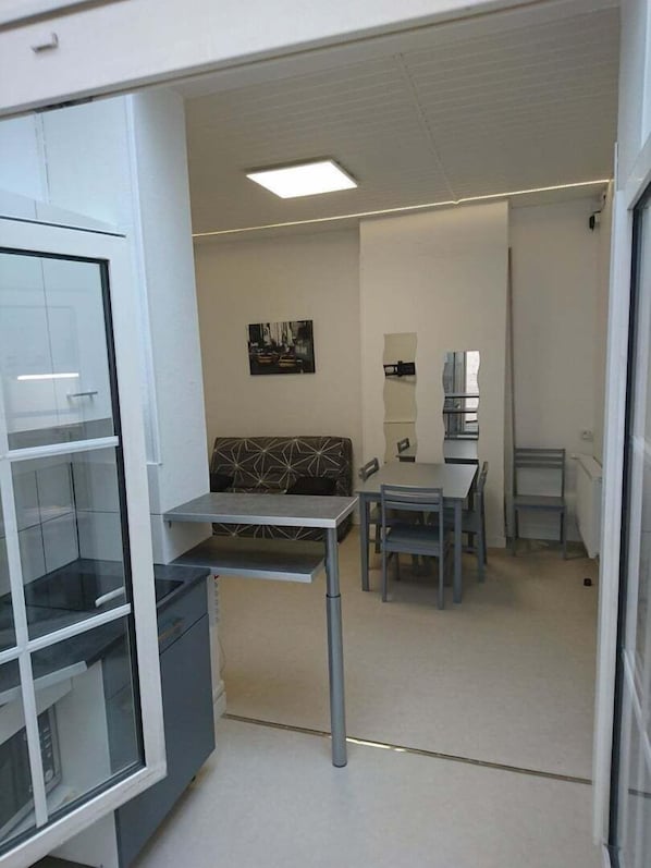 A modern office space with a glass partition, a sofa, a table with chairs, and a painting on the wall.
