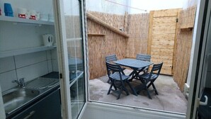 Eine kompakte Küche mit Spüle und Regalen, ein kleiner Essbereich mit Tisch und Stühlen sowie eine Holzwand.