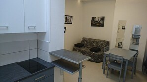 Eine kompakte Küchenzeile mit eingebautem Herd, einem kleinen Tisch und einer Couch mit gemusterten Kissen.