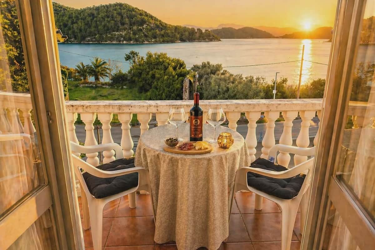 Un balcón con una mesa dispuesta para dos personas, con vistas panorámicas a un lago y montañas al atardecer.