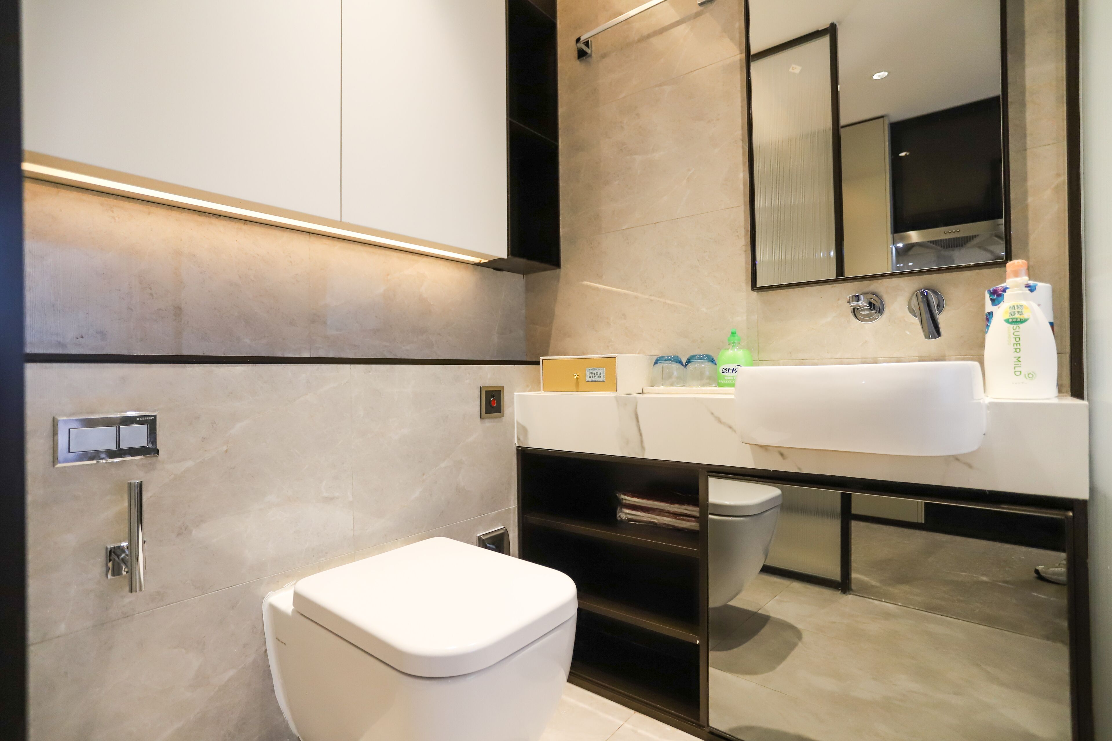 A modern bathroom with a white toilet, a sink with a mirror above it, and a shelf with toiletries.
