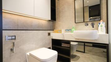 A modern bathroom with a white toilet, a sink with a mirror above it, and a shelf with toiletries.