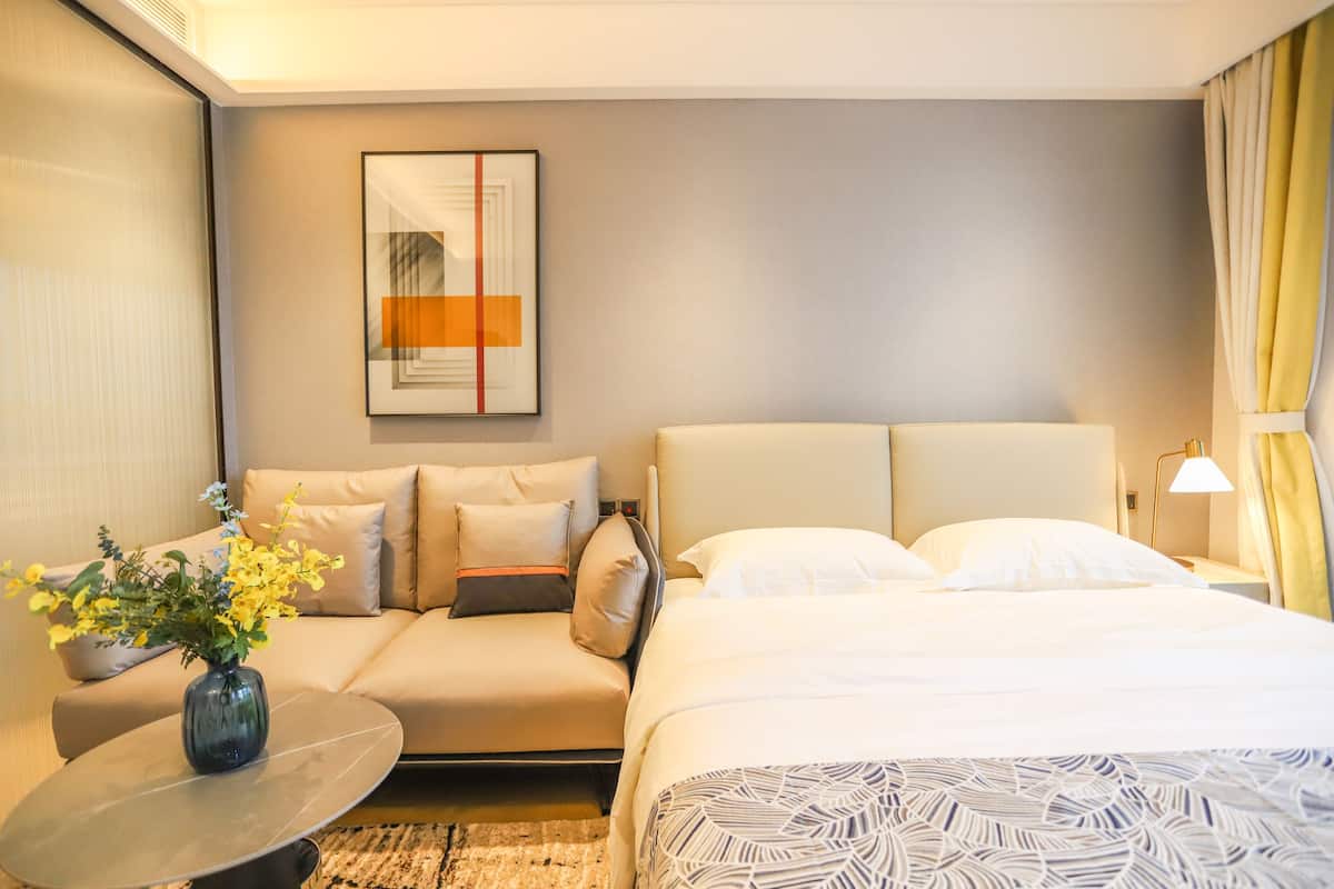 Habitación de hotel con cama, sofá, una mesita con un florero y un cuadro en la pared.