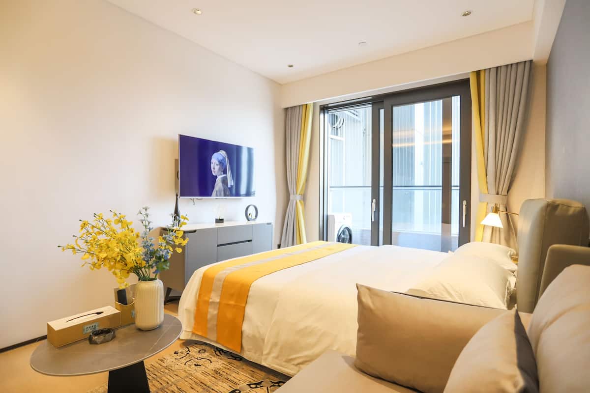 Habitación de hotel con una cama grande, un televisor de pantalla plana en la pared, un escritorio con lámpara y una ventana con cortinas.