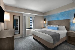 A modern hotel room with a large bed, a bedside table, a nightstand, a mirror, and a window with curtains.