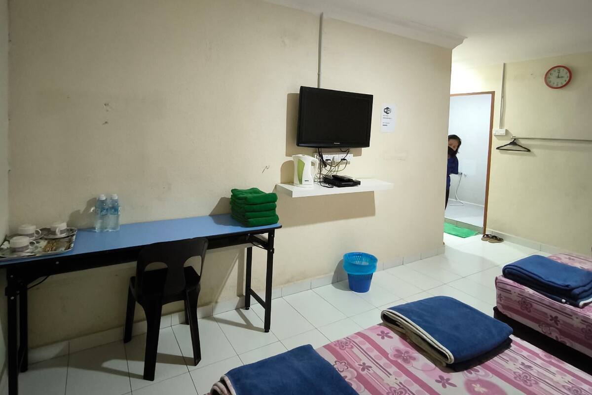 Une chambre d’hôtel équipée d’un bureau, d’une chaise, de deux lits, d’une télévision, et dont on aperçoit la salle de bain à l’arrière-plan.
