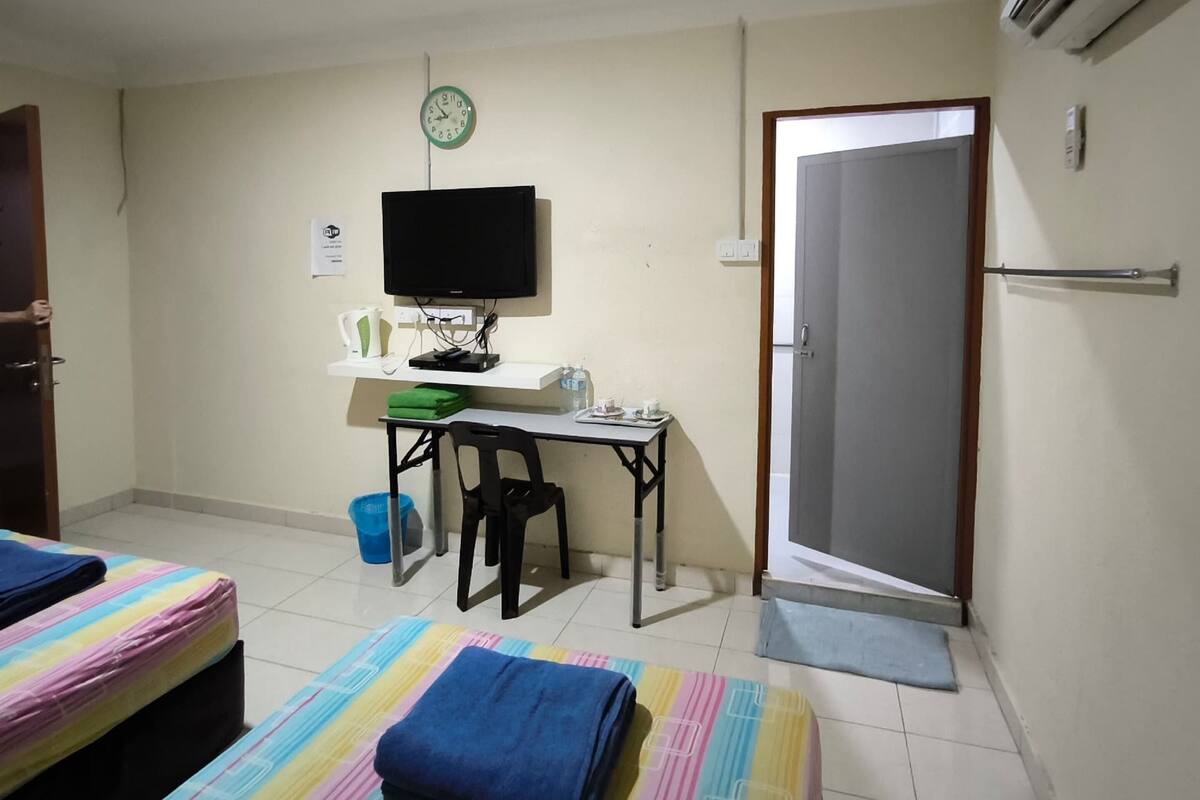 Une chambre avec deux lits, un bureau avec un ordinateur, une horloge et un appareil de climatisation.