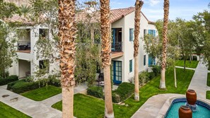 A multi-story building with a pool, surrounded by palm trees and well-maintained lawns.