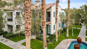 A multi-story building with a pool, surrounded by palm trees and well-maintained lawns.