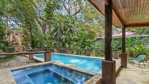 A rectangular pool with a stone border, surrounded by lush greenery and a wooden pergola. - Stylish 3-Bedroom Tropical Escape with Pool & Outdoor Living, 1 Block from Playa Potrero (Playa Potrero)