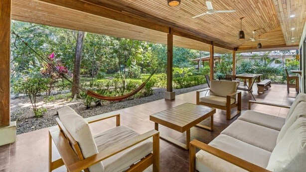 An outdoor patio with wooden furniture, a hammock, and a view of a lush garden. - Stylish 3-Bedroom Tropical Escape with Pool & Outdoor Living, 1 Block from Playa Potrero (Playa Potrero)