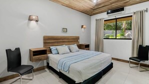 A bedroom with a wooden ceiling, a bed with a blue-striped bedspread, two bedside tables, a wall-mounted lamp, and a window with curtains. - Stylish 3-Bedroom Tropical Escape with Pool & Outdoor Living, 1 Block from Playa Potrero (Playa Potrero)