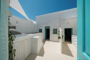 A white-walled building with multiple doors and windows, a balcony with plants, and a clear blue sky. - Marla Luxury Residences (Santorini)