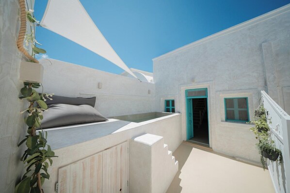 A white-walled room with a bed, a window, and a door. - Marla Luxury Residences (Santorini)