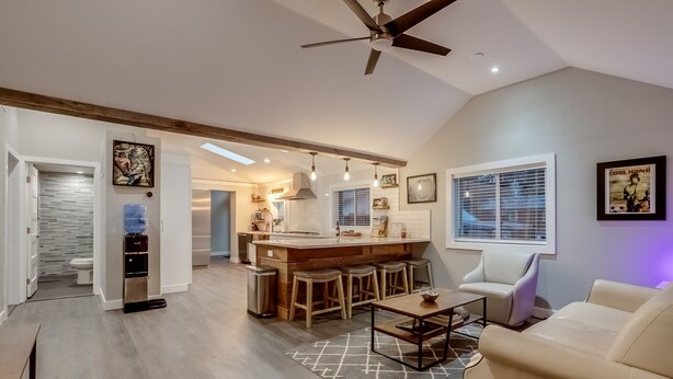 A modern kitchen with a central island, bar stools, and a ceiling fan.