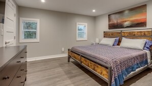A bedroom with a bed, dresser, and two windows.
