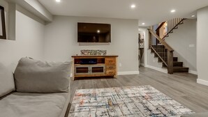 A modern living room with a sofa, a wooden cabinet, a TV, and a staircase.
