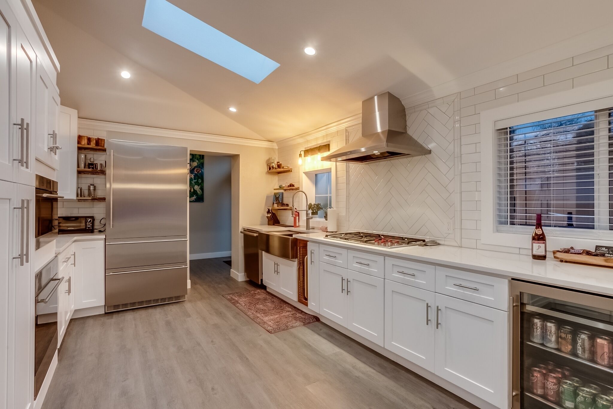 Una cocina moderna con armarios blancos, un refrigerador de acero inoxidable, horno empotrado y una ventana con persianas.