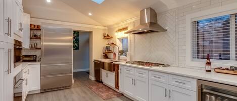Una cocina moderna con armarios blancos, un refrigerador de acero inoxidable, horno empotrado y una ventana con persianas.