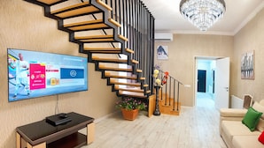 A modern living room with a wooden staircase, a flat-screen TV, a bench, and a potted plant. - H&B apartments Agmashenebeli II (Tbilisi)