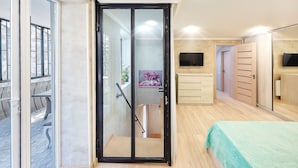 A bedroom with a sliding door leading to a balcony, a bed with a green bedspread, a TV mounted on the wall, and a wooden wardrobe. - H&B apartments Agmashenebeli II (Tbilisi)