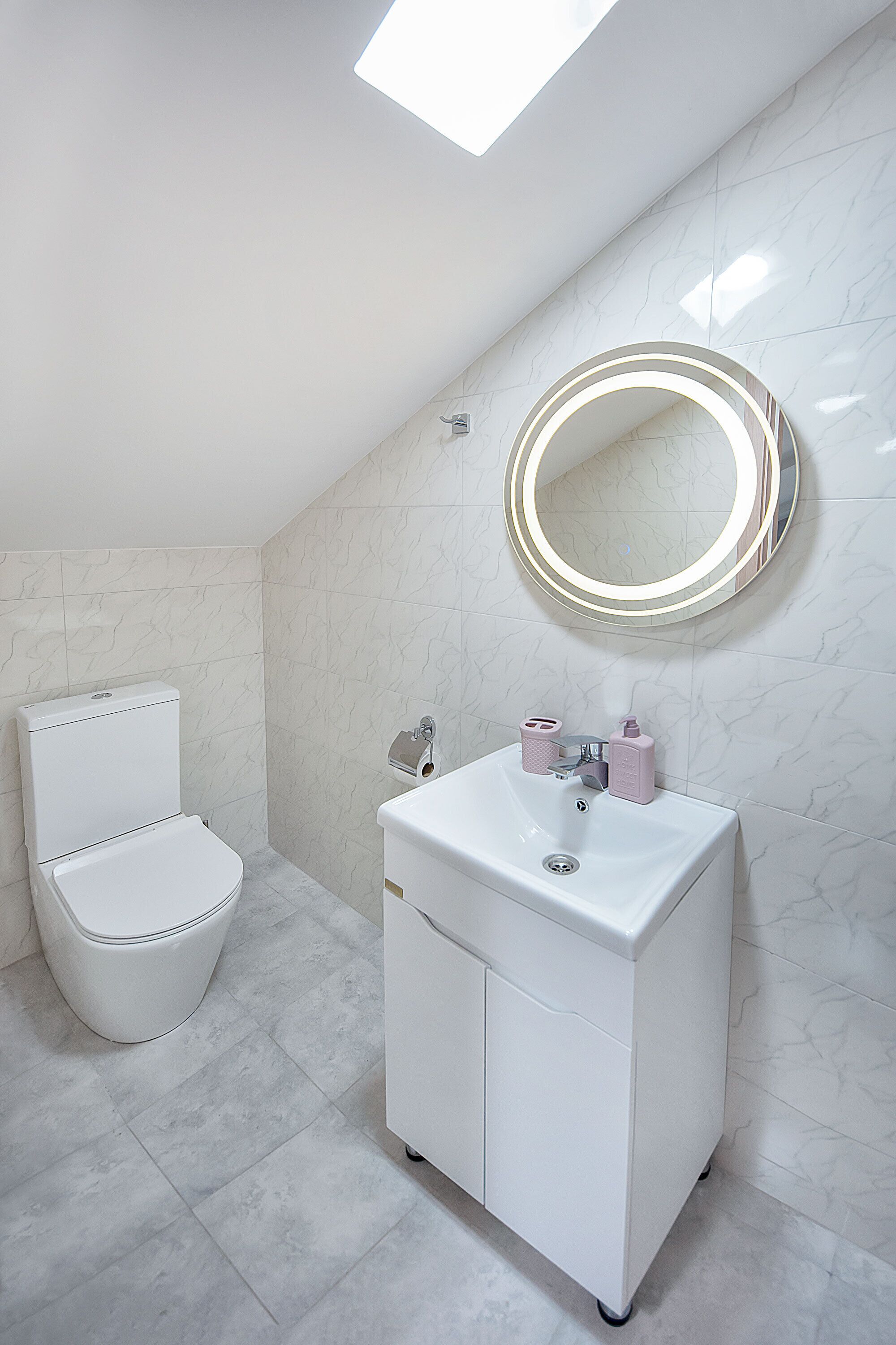 A bathroom with a toilet, a sink, and a mirror with lights.
