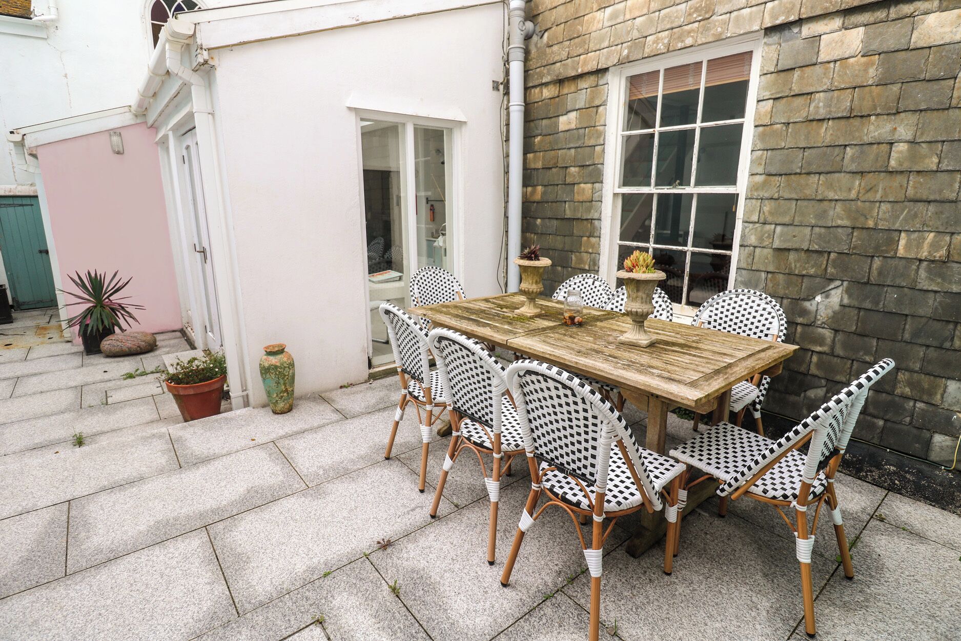 Un patio exterior con una mesa de madera y sillas de mimbre blanco.