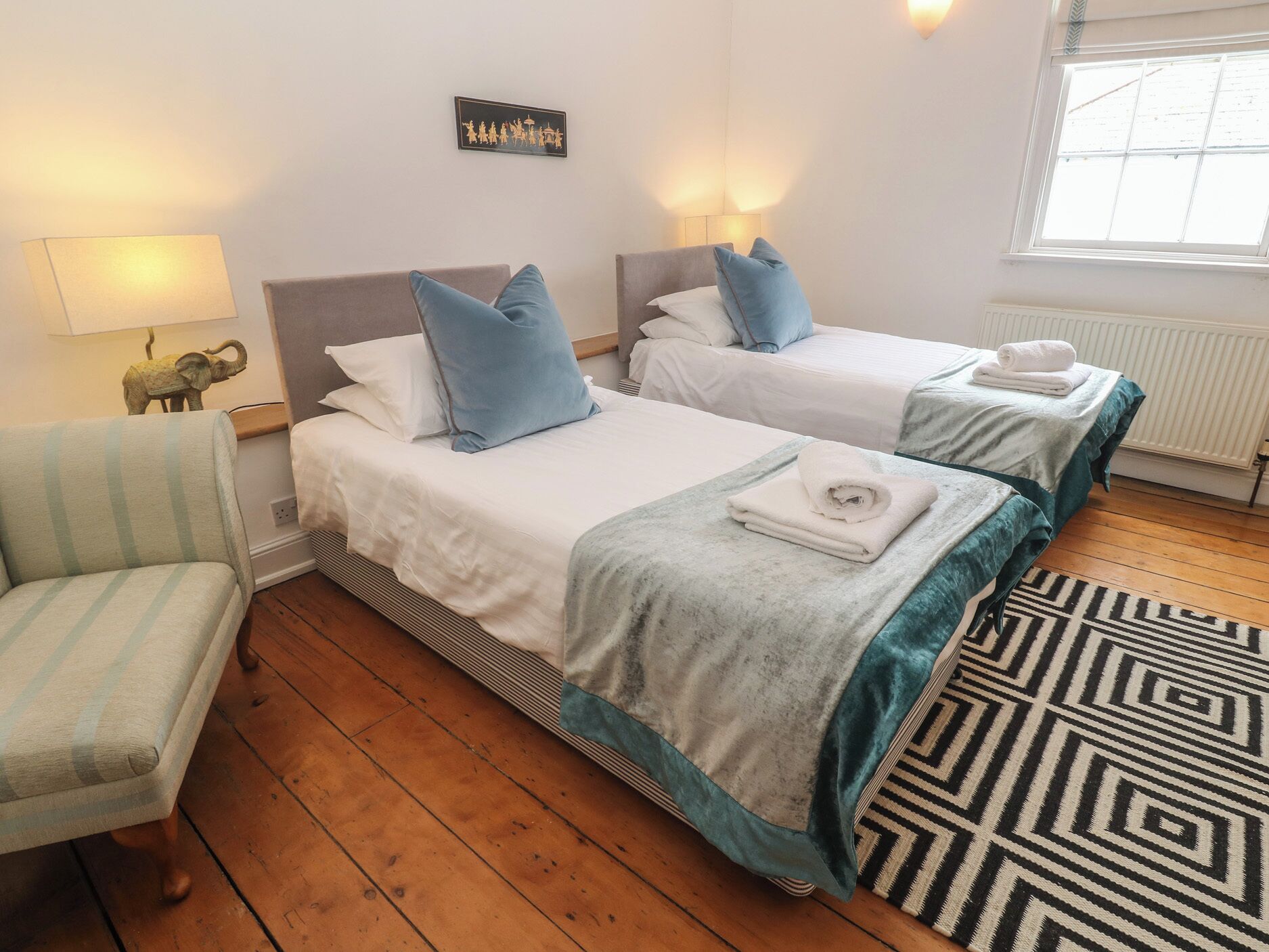 A hotel room with two beds, a chair, a patterned rug, and a wall-mounted picture.